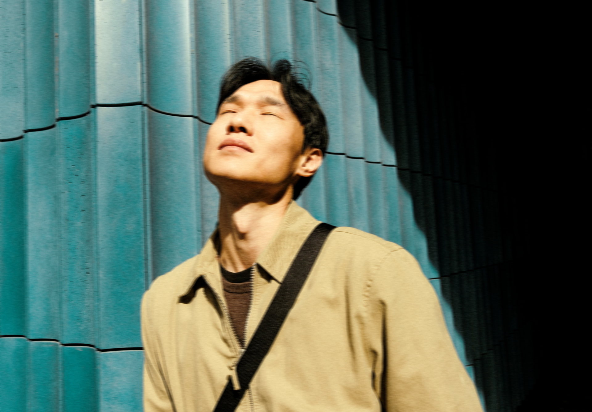 Man in a jacket standing against a teal wall in warm sunlight
