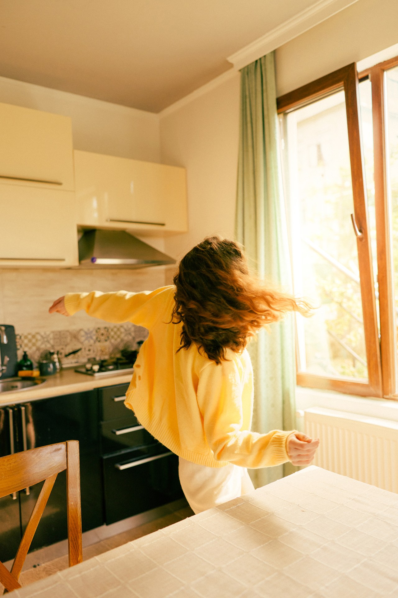 Woman in a yellow sweater dancing in a sunlit kitchen